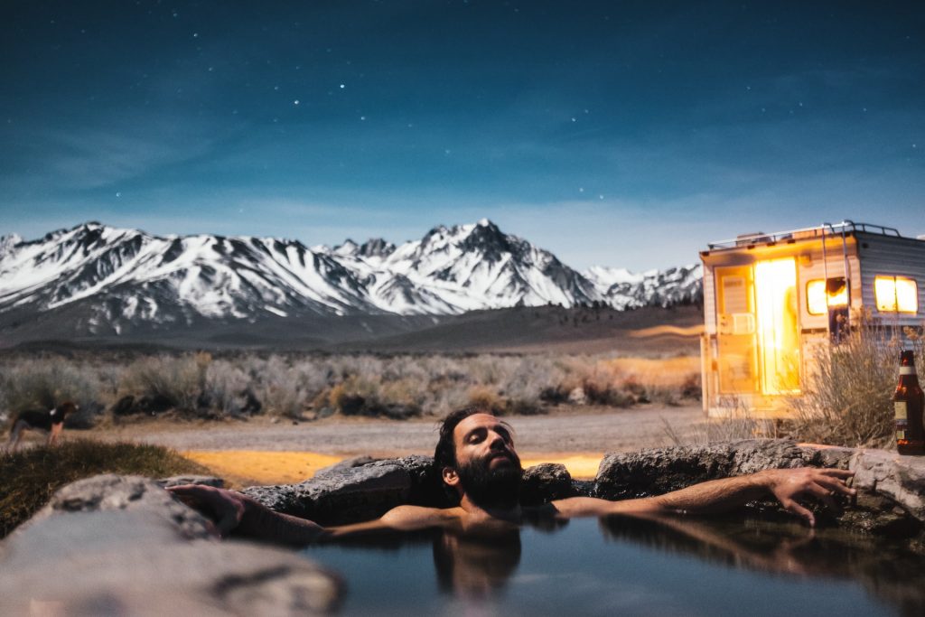 man relaxing in a hot springs with utah mountains shown behind him