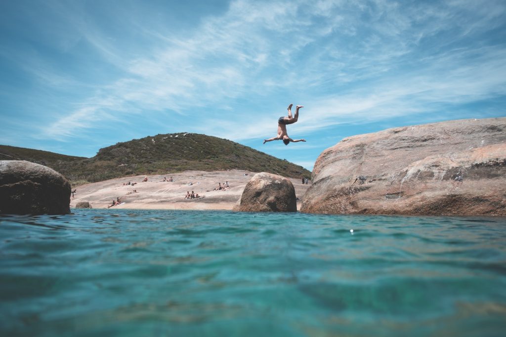 man doing a flip off a rock into the beach water